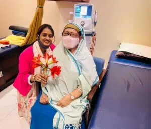 Dr. Tazia Sardar presenting a bouquet of flowers to a female patient celebrating a successful rehabilitation milestone inside a Back in Motion clinic treatment room in Dhaka.