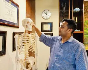 Dr. Md. Abdullah Yousuf, Chief Medical Consultant, pointing to a human skeleton model to explain joint and spine anatomy inside a Back in Motion clinic room in Dhaka.