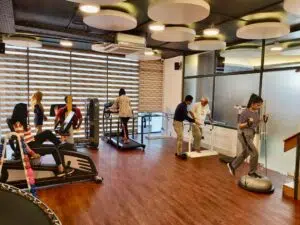 Wide-angle view of the active Back in Motion rehabilitation clinic in Dhaka, featuring physical therapists assisting patients with treadmill gait training and balance exercises. Clearly describes the clinical activity and environment for screen readers and search bots, including your brand name and location. Title Back in Motion